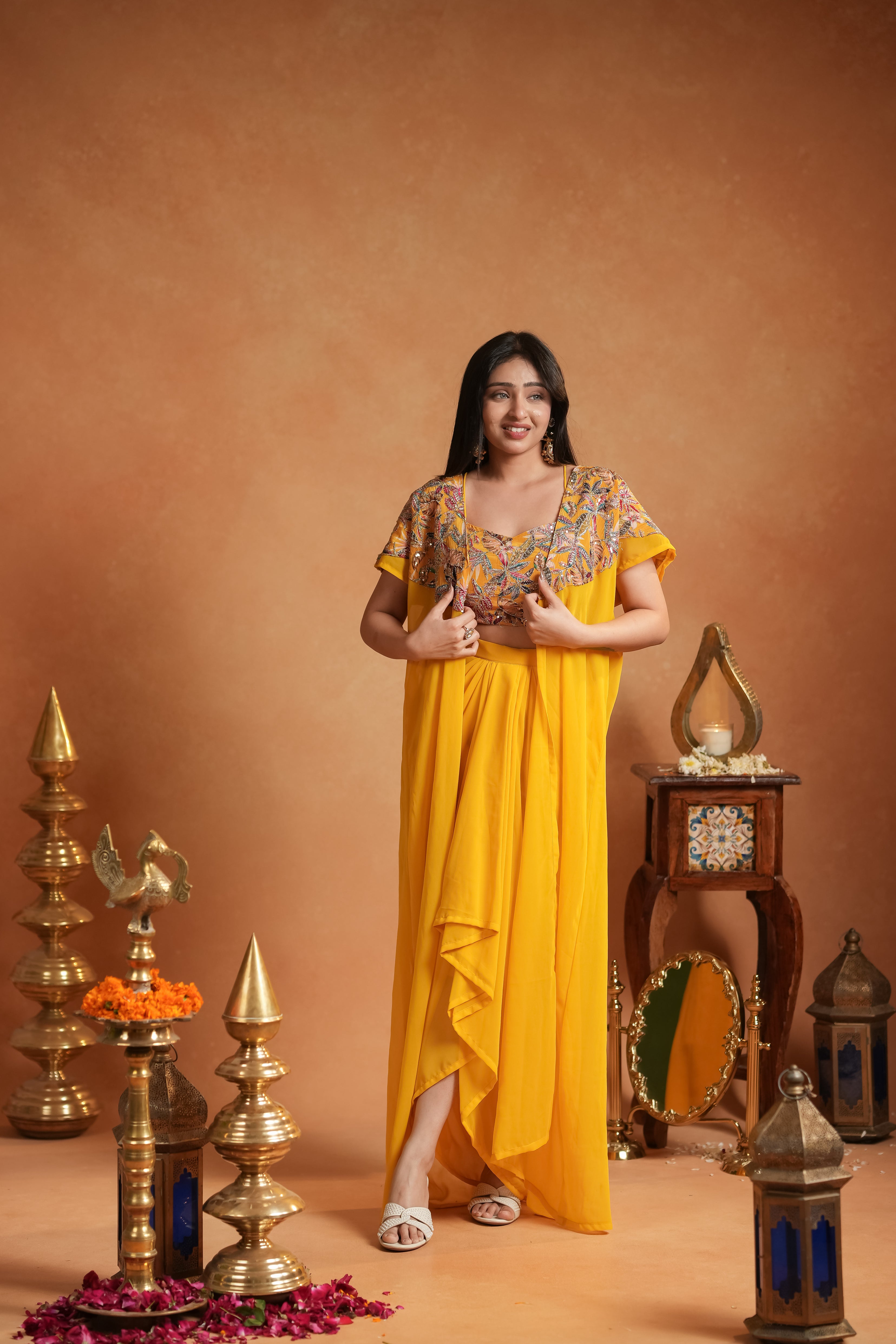 Woman in a yellow dress standing in front of decorative items on a brown background